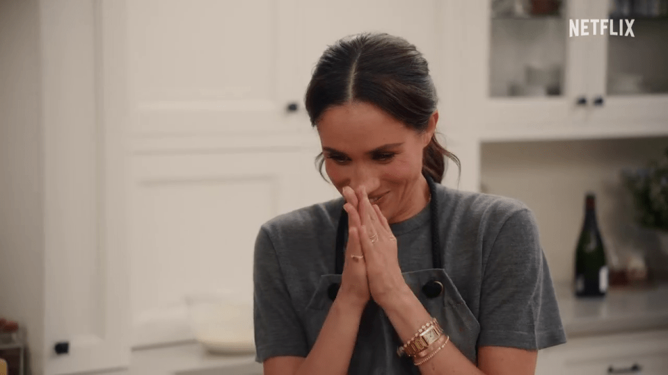 Meghan Markle smiling with hands clasped.