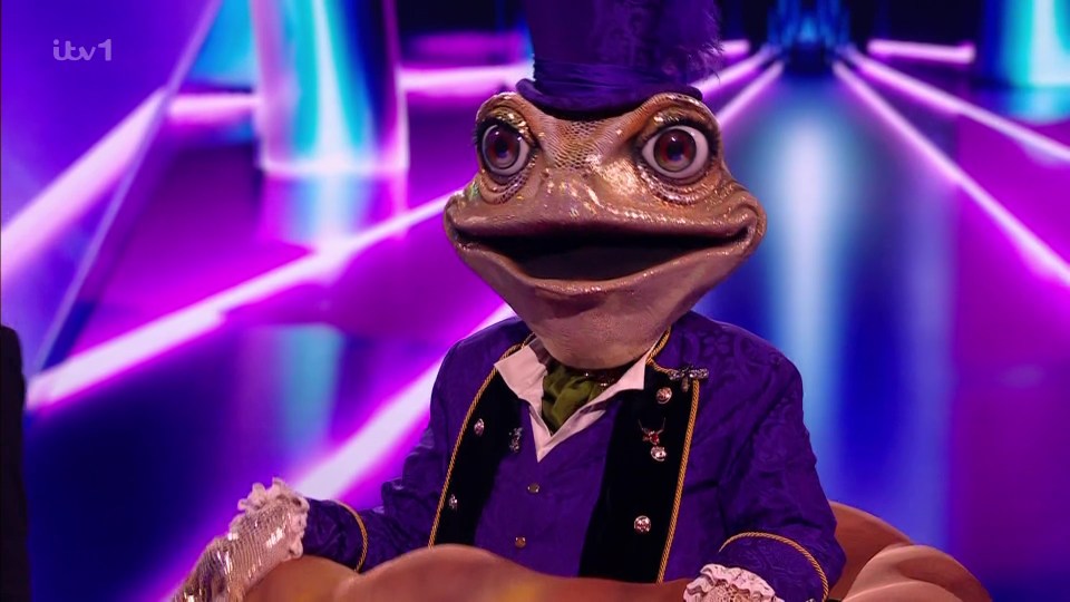 Frog in a purple suit and top hat on a game show.