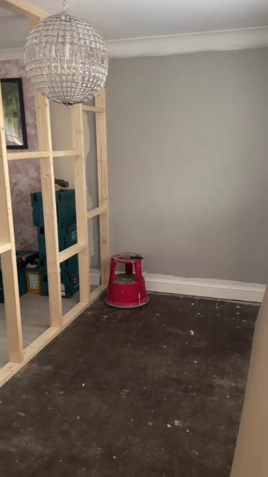 Room undergoing renovation with a partially built wall and a chandelier.