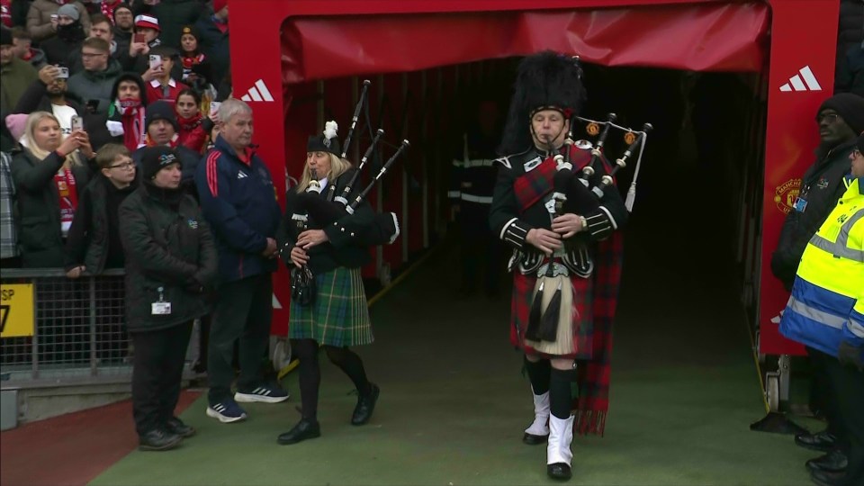 Two bagpipers in kilts walking through a stadium tunnel.