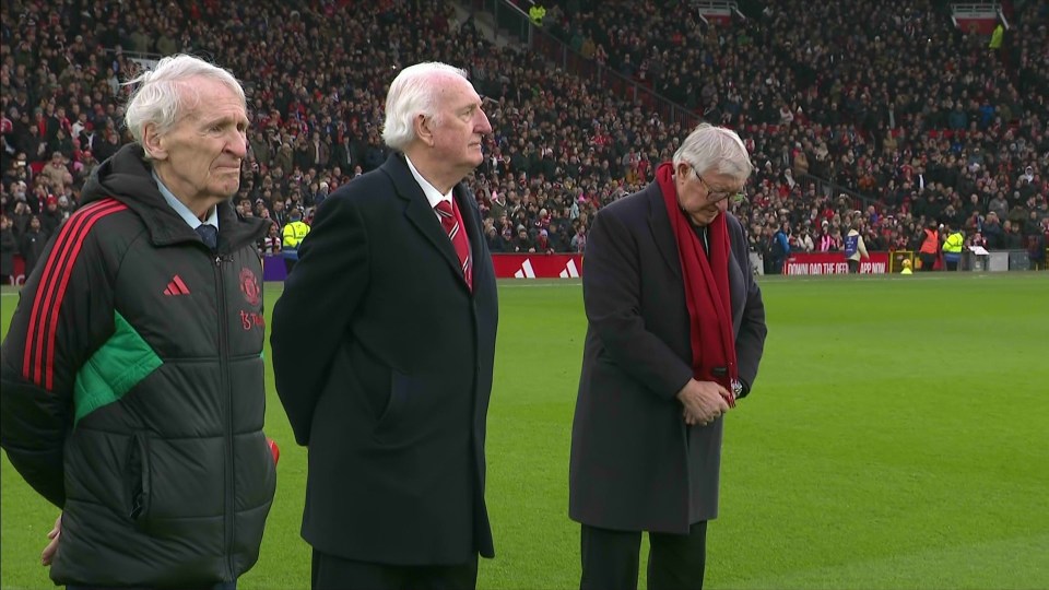 Three men standing on a soccer field in front of a crowd.