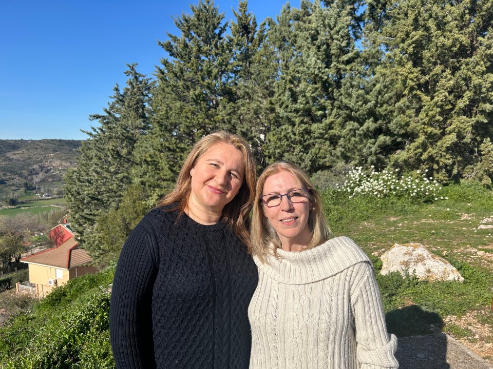 Two women stand outdoors, smiling for a photo.