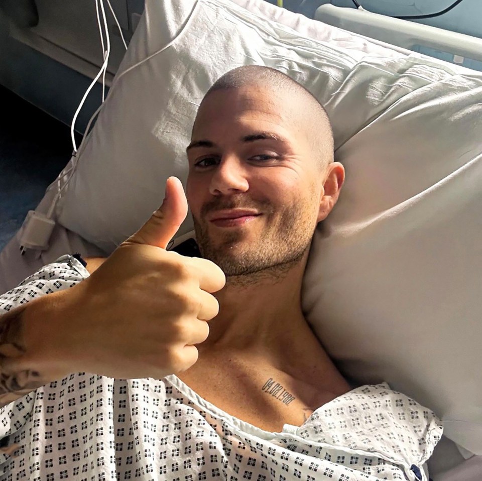 Max George in a hospital bed giving a thumbs up.