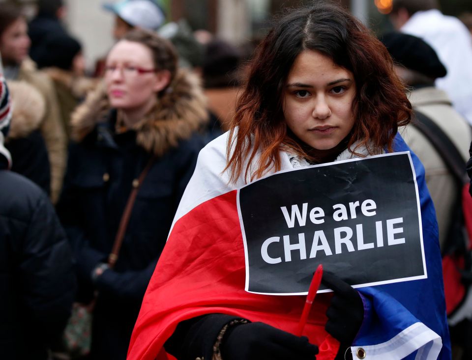 A woman wearing a French national flag holds a ‘We are Charlie’ sign during a march