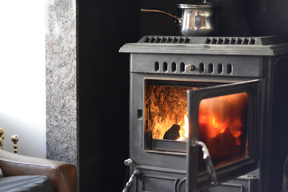 A black wood-burning stove with a fire burning inside and a pot simmering on top.