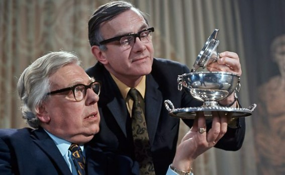 Two men examining a silver bowl on a tray.