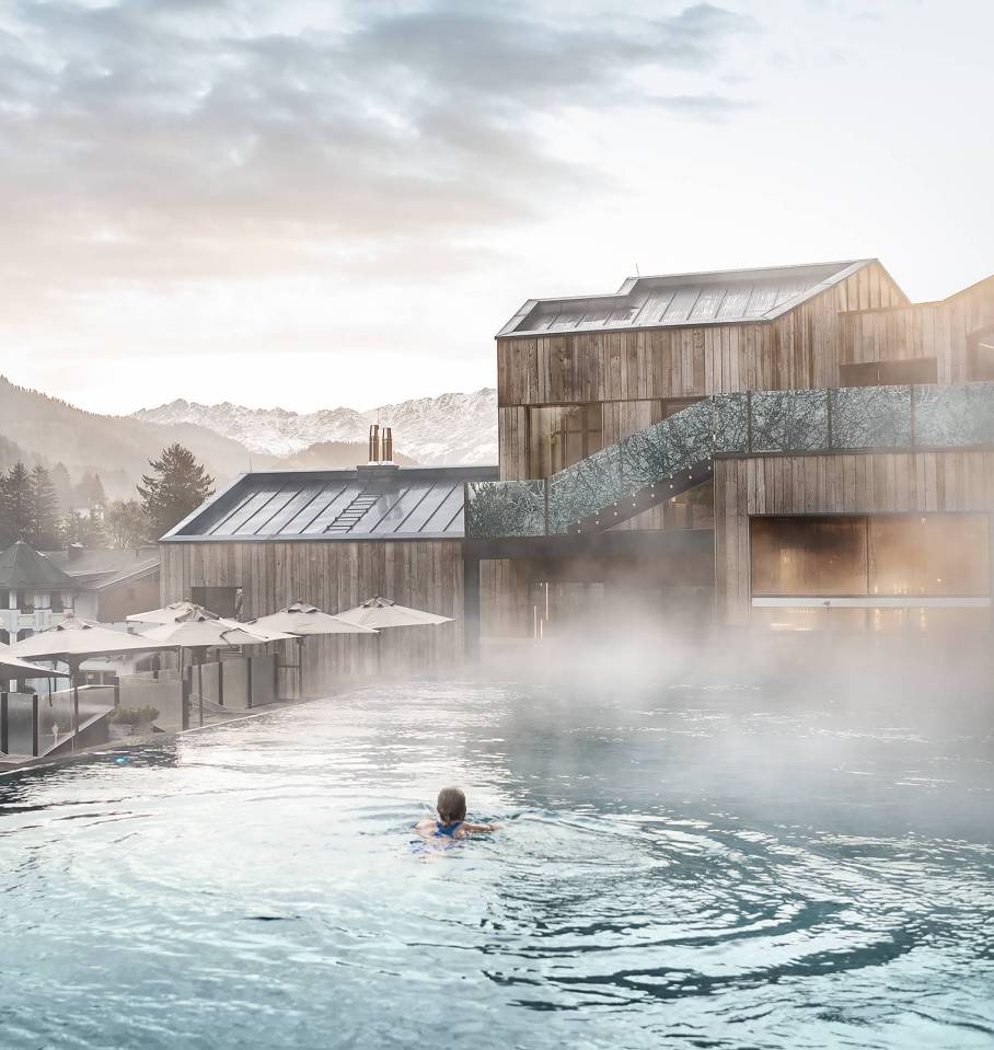 Person swimming in an outdoor pool at a spa with a mountain view.