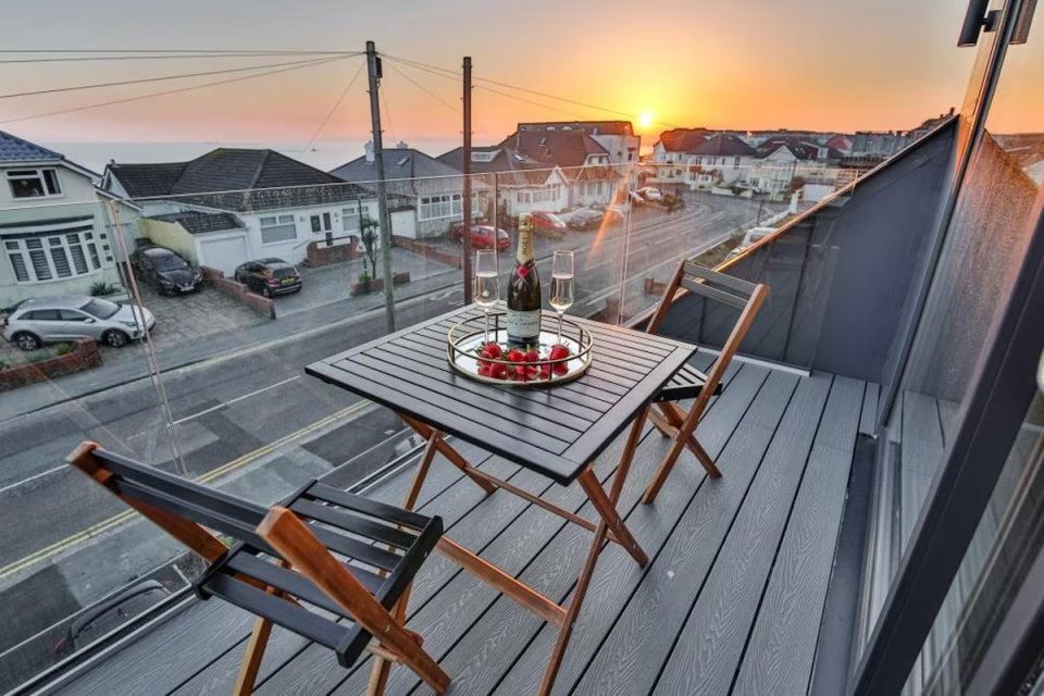 Balcony table with champagne and strawberries at sunset overlooking houses and the sea.