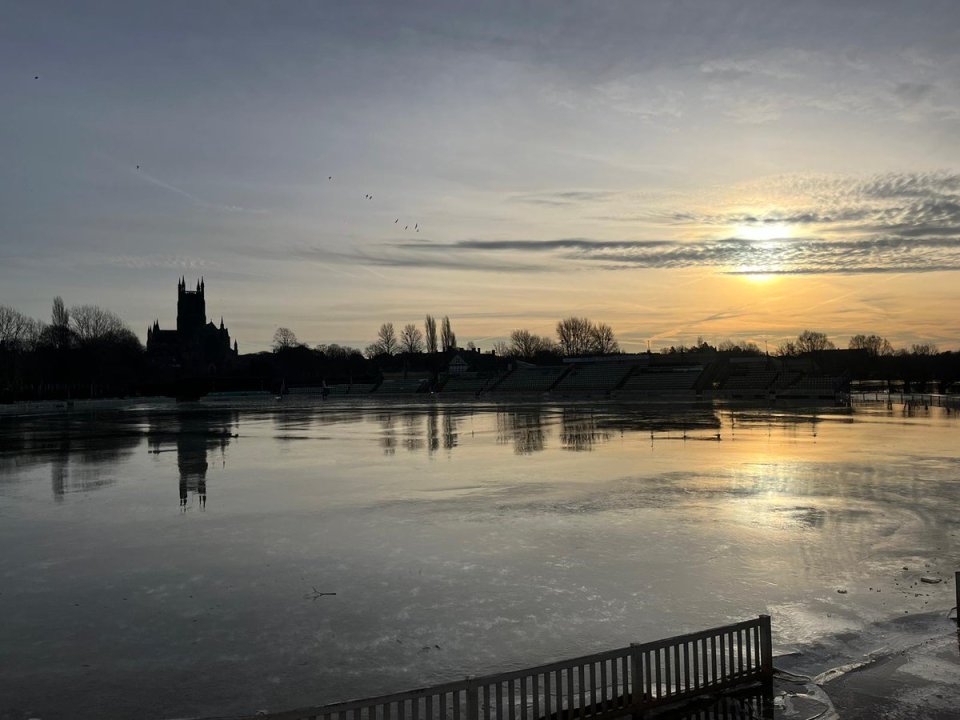 Sunset over a flooded cricket ground with a church in the background.