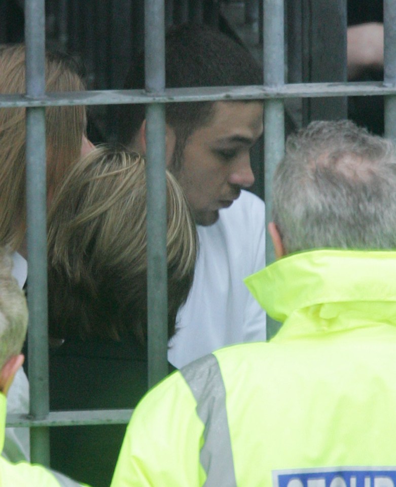 A young man in a white shirt, seen through a metal cage, at a court hearing.