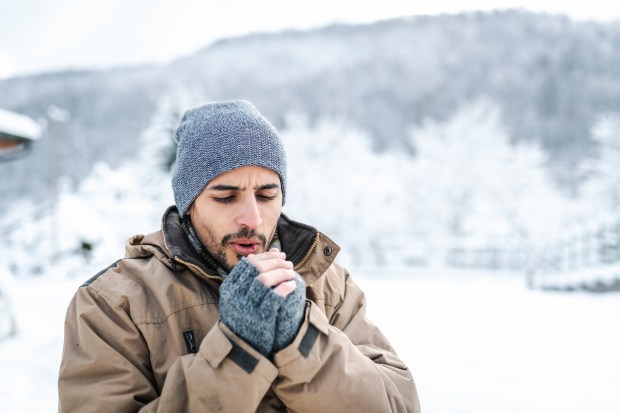 Man in winter coat warming his hands in the snow.